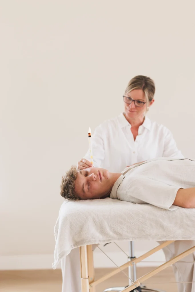 Eveline Grasmuck bei der Anwendung von einer Körperkerze an einem jüngeren Herrn, der auf einer Liege liegt